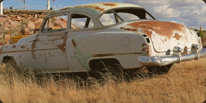 A rusted 1950s Oldsmobile sitting in tall dry grass beside Route 66
